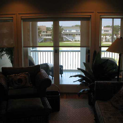 Living room with solar shades partially drawn, showcasing an outdoor balcony view through large glass doors.